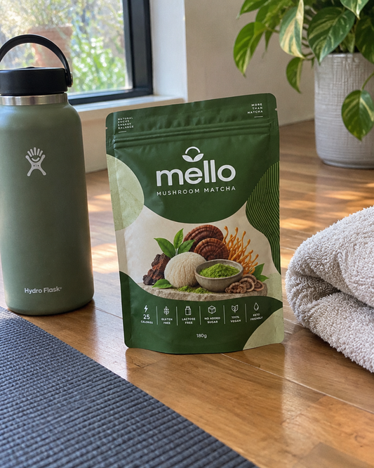 Mello Mushroom Matcha pouch on a wooden floor beside a water bottle, a folded towel and a yoga mat