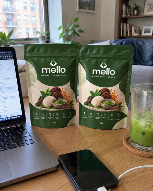 Two Mello Mushroom Matcha pouches on a desk beside a laptop and an iced matcha latte