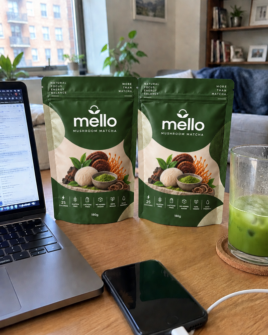 Two Mello Mushroom Matcha pouches on a desk beside a laptop, a phone and an iced matcha