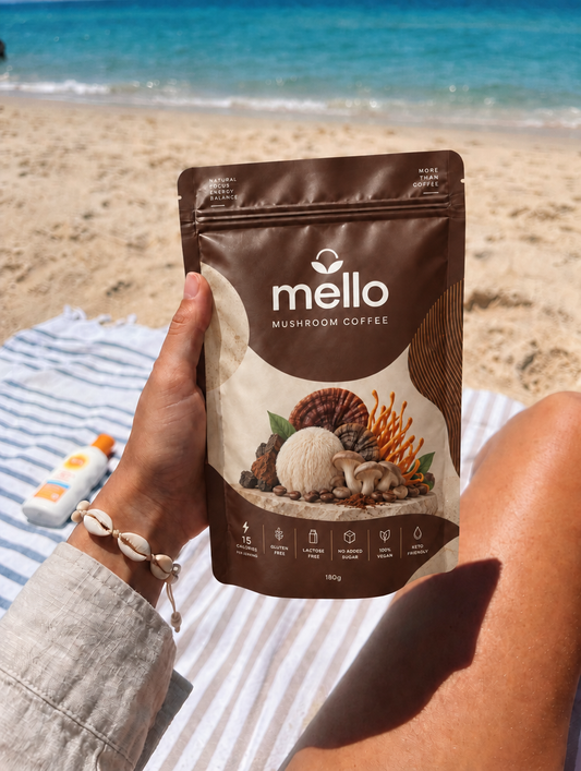 Mello Mushroom Coffee pouch held up on a striped towel at the beach with the sea behind